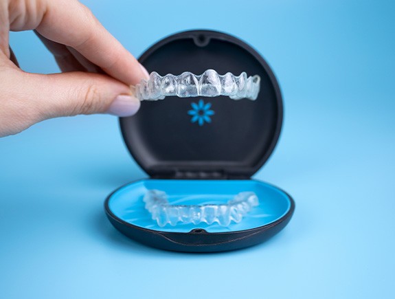 Fingers picking up Invisalign from carrier case on blue surface