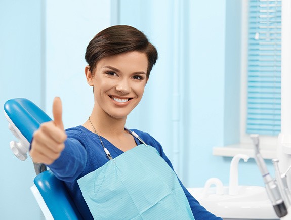 Female dental patient sitting in chair and giving a thumbs up