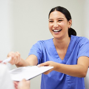 Woman in blue scrubs handing paperwork on clipboard and pen to patient