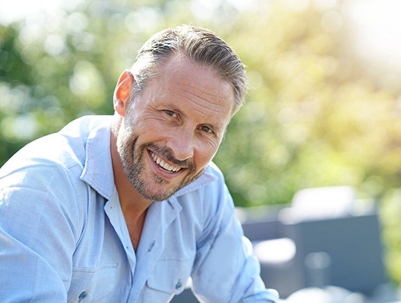 Man in button-up shirt sitting outside smiling