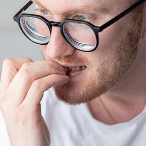 Man with glasses biting his fingernails