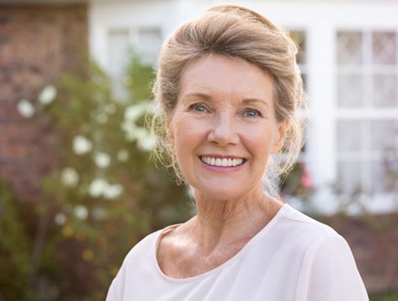 Senior woman in white shirt standing outside of house